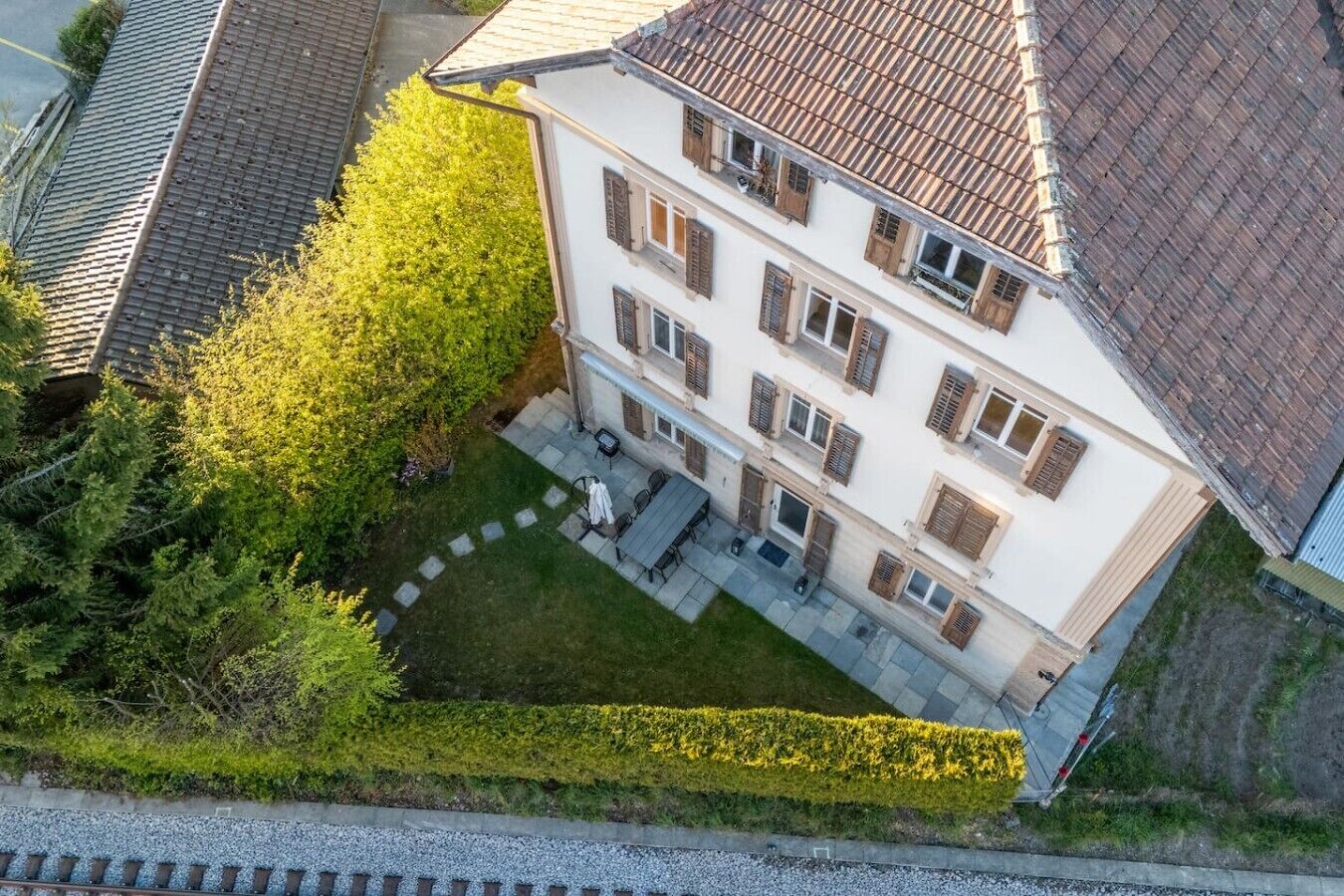 Ein mehrstöckiges Gebäude mit Innenhof, gepflasterter Terrasse und einer Hecke.