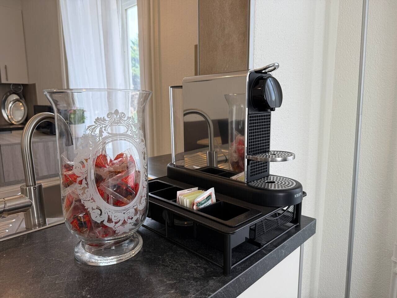 Un comptoir de cuisine avec une machine à café, un récipient en verre contenant des objets rouges et un petit appareil électroménager.
