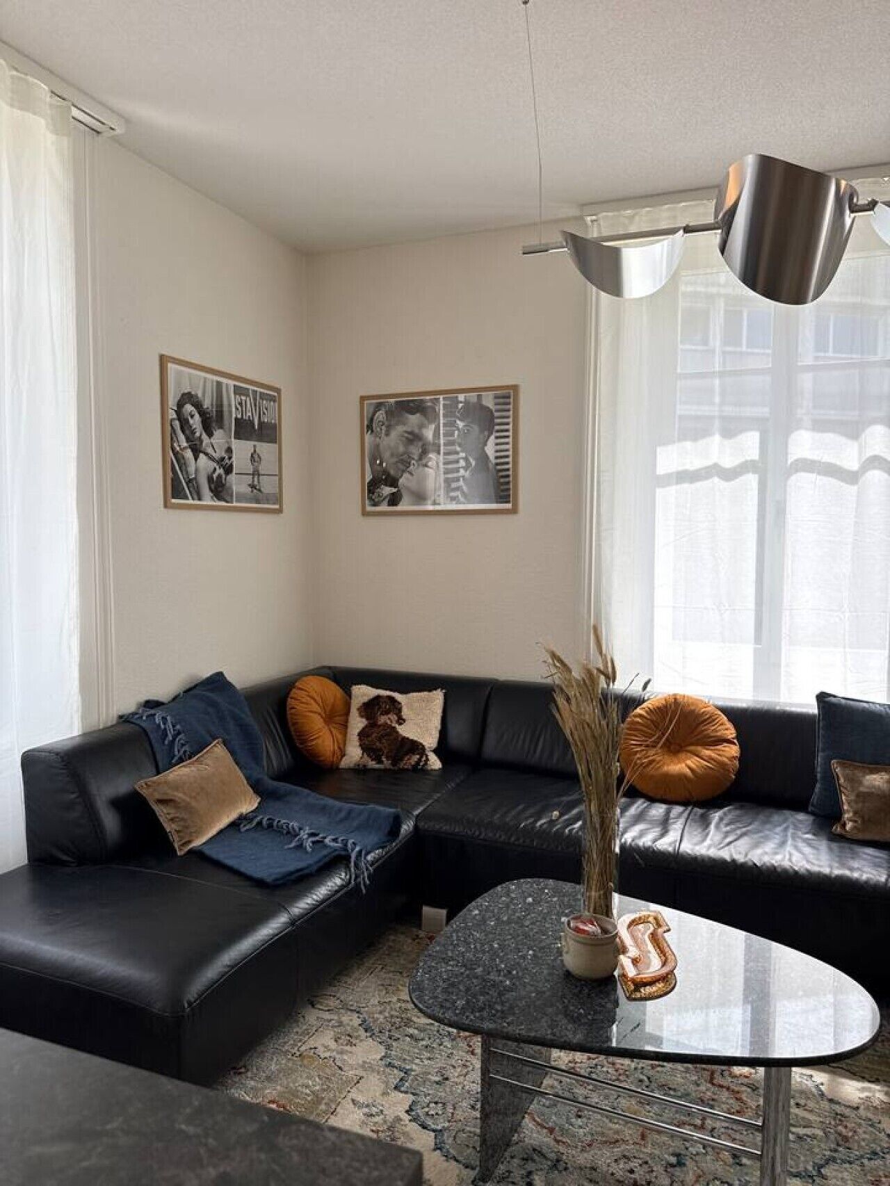 Een moderne woonkamer met een zwarte leren bank, een ronde salontafel en twee ingelijste foto’s aan de muur.
