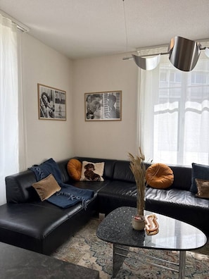 A modern living room with a black leather sofa, a round coffee table, and two framed pictures on the wall. - Spacious apartment with a private garden and entrance (Huttwil)
