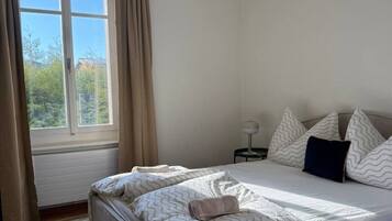 A bedroom with a bed, a nightstand, a lamp, and a window with curtains.