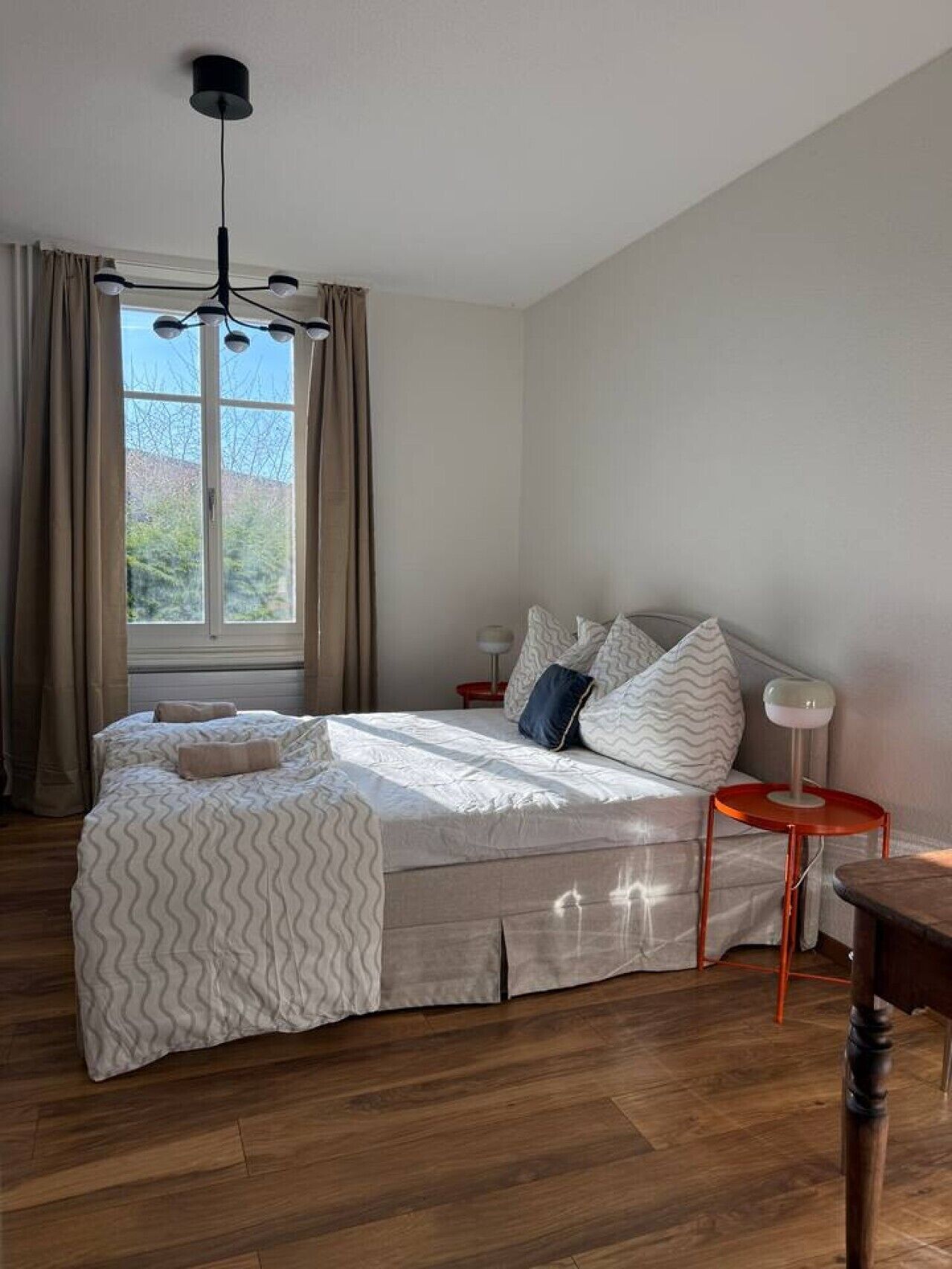 Une chambre à coucher avec un lit, une table de chevet, une lampe et une fenêtre avec des rideaux.