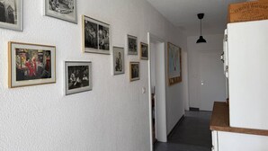 A hallway with framed photographs on the walls, a white refrigerator, and a wooden counter. - Spacious apartment with a private garden and entrance (Huttwil)
