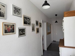 Ein Flur mit gerahmten Fotografien an den Wänden, einem weißen Kühlschrank und einer Holzauslage.