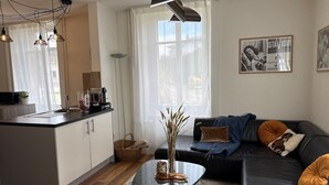 A modern living space with a kitchen island, a black sofa with cushions, and a coffee table with a vase. - Spacious apartment with a private garden and entrance (Huttwil)