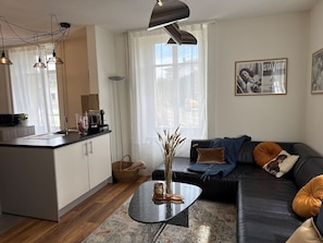 Ein zeitgemäßer Wohnraum mit Kücheninsel, einer schwarzen Couch mit Kissen und einem Couchtisch mit einer Vase.