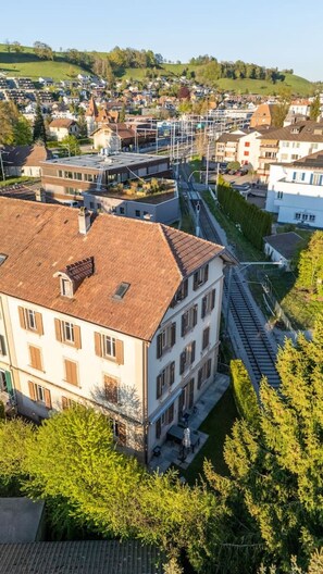 Ein mehrstöckiges Gebäude mit flachem Dach, neben einer Bahntrasse, umgeben von Grünflächen und weiteren Wohngebäuden.