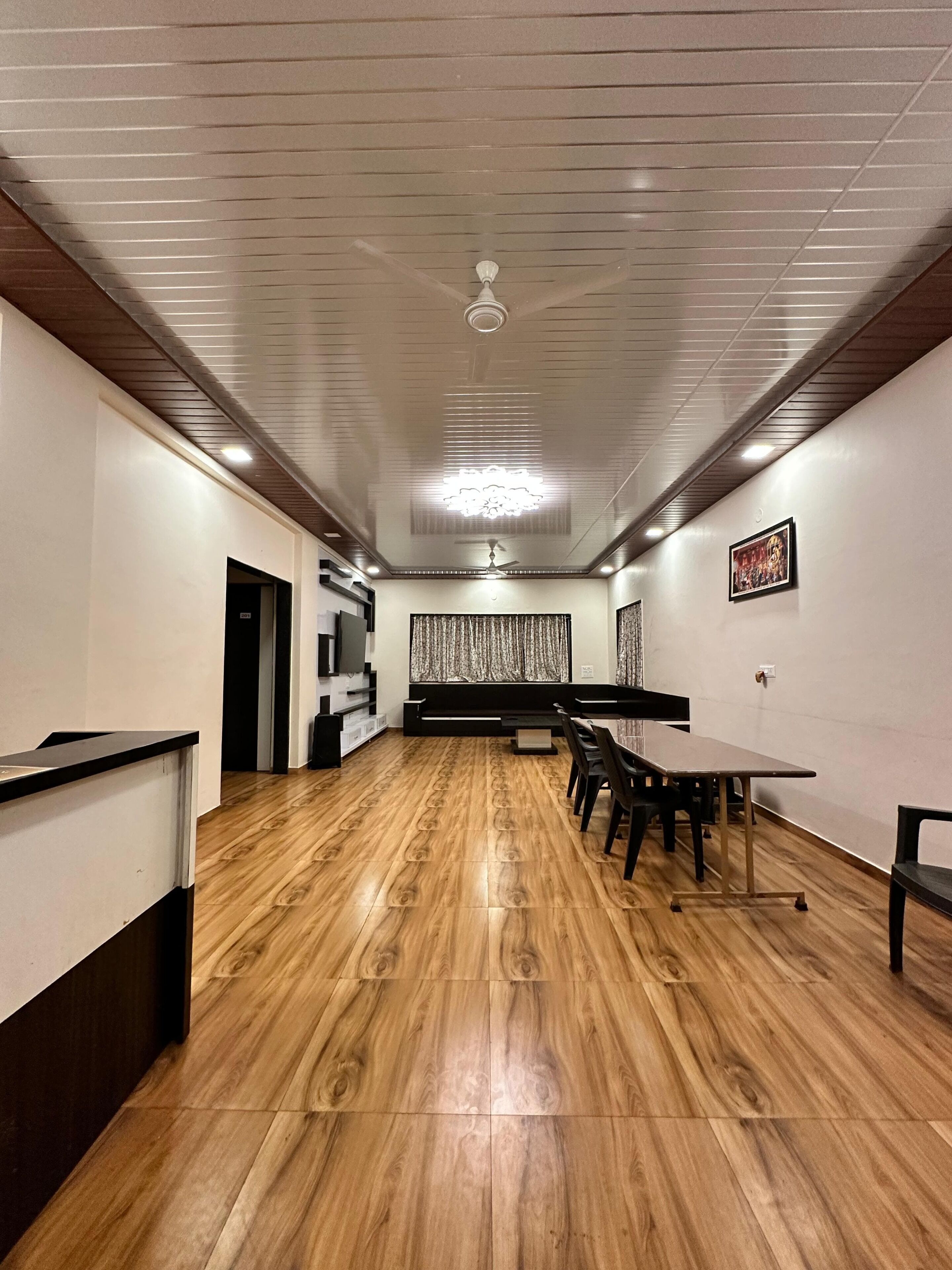 Une salle de conférence avec une longue table, des chaises, un ventilateur de plafond et un rideau à motifs.