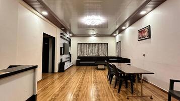 Une salle de conférence avec une longue table, des chaises, un ventilateur de plafond et un rideau à motifs.