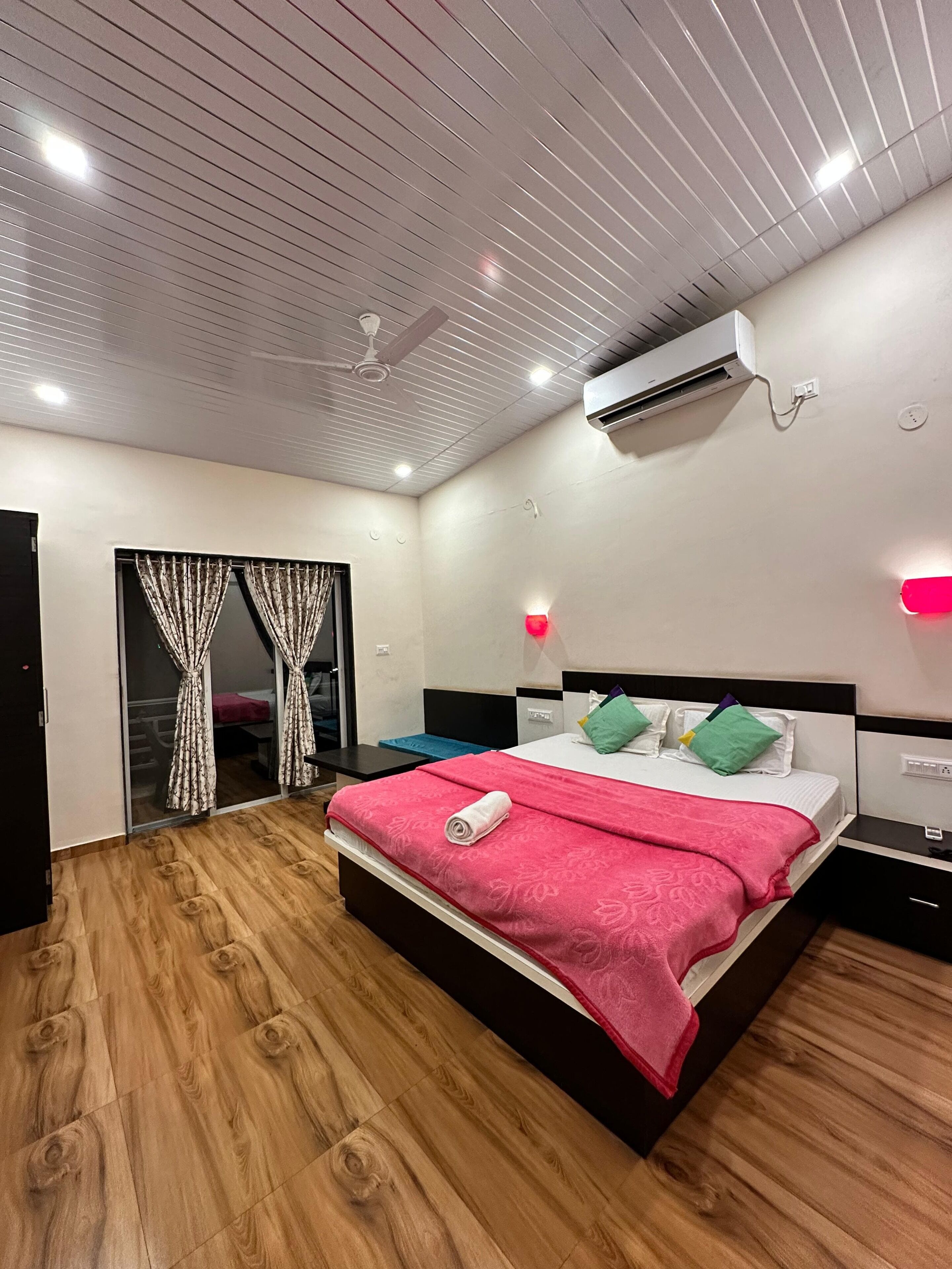 A modern bedroom with a wooden floor, a bed with a red blanket, a ceiling fan, and an air conditioning unit.