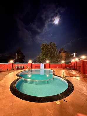 A swimming pool with a surrounding deck, a red brick wall, and a view of the sky.