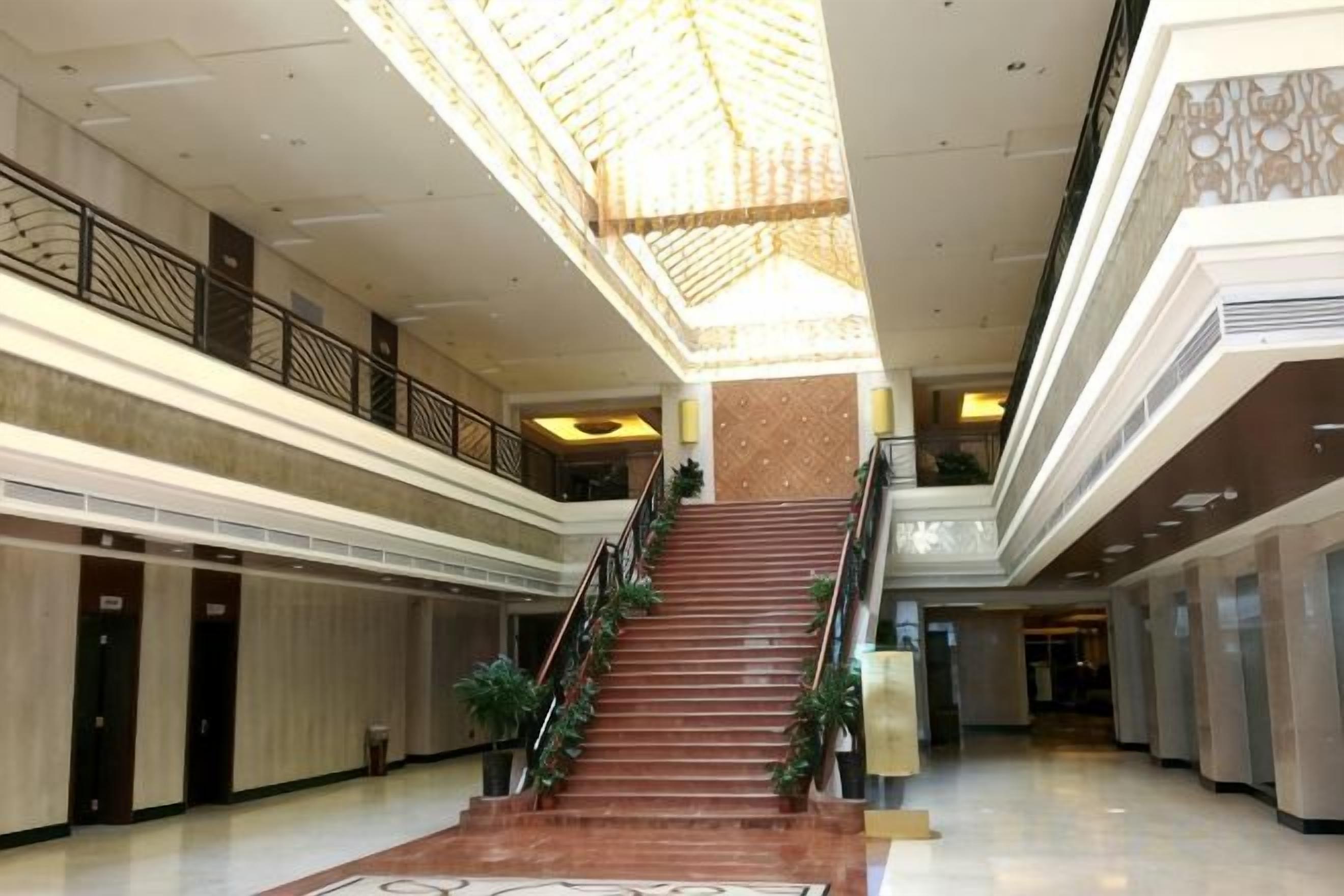 A spacious atrium with a central staircase, multiple levels, and a high ceiling with a decorative pattern.