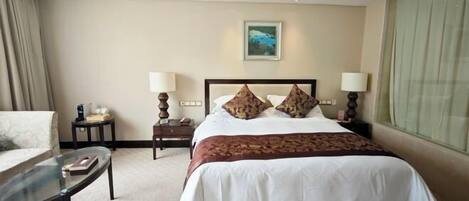 A hotel room with a large bed, two bedside tables, a chair, and a window.