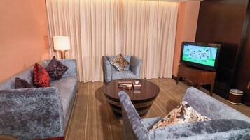 Habitación de hotel con sofá, sillones, una mesa de centro, televisor y cortina.
