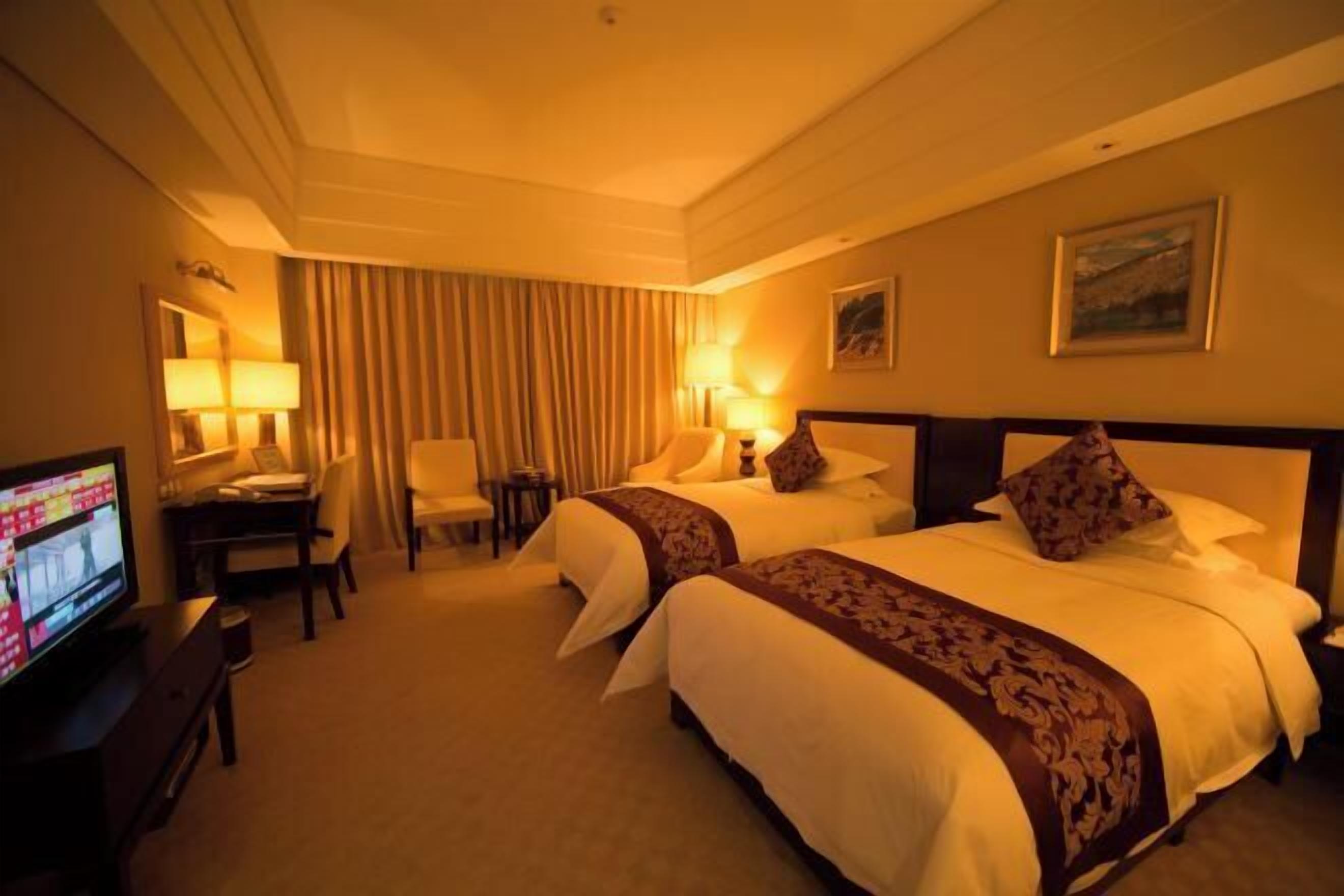 A hotel room with two beds, a desk, a chair, a television, and a large window.