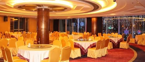 A banquet hall with round tables, chairs, and a red carpet.