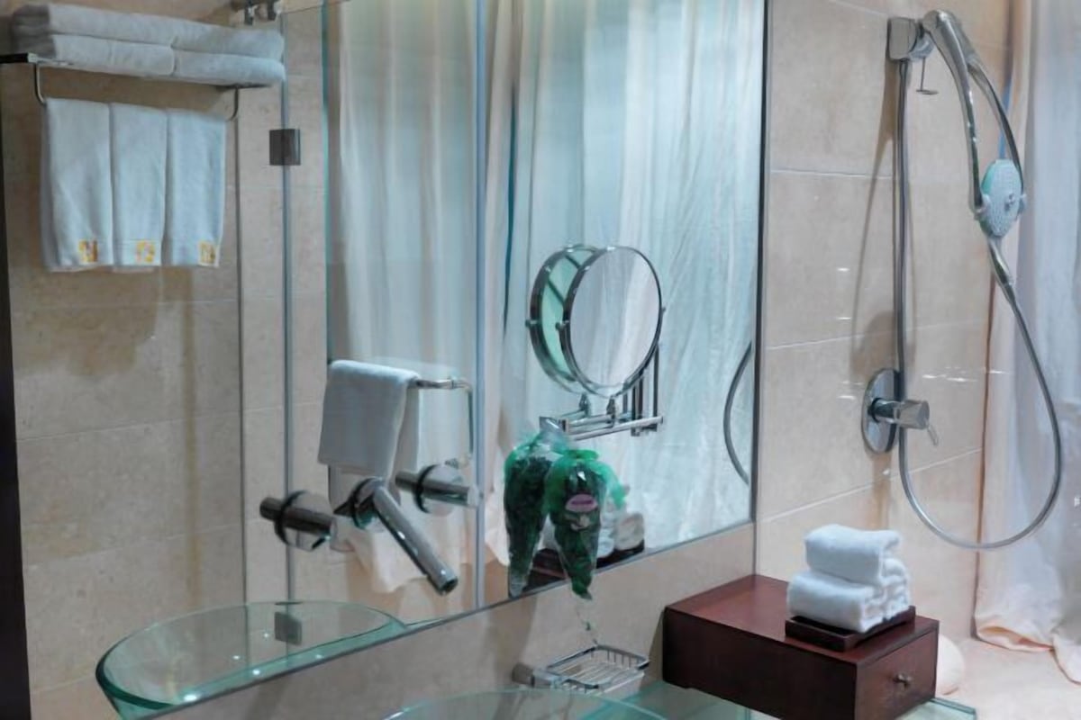 A bathroom with a glass shower enclosure, a handheld showerhead, a towel rack, and a glass sink.