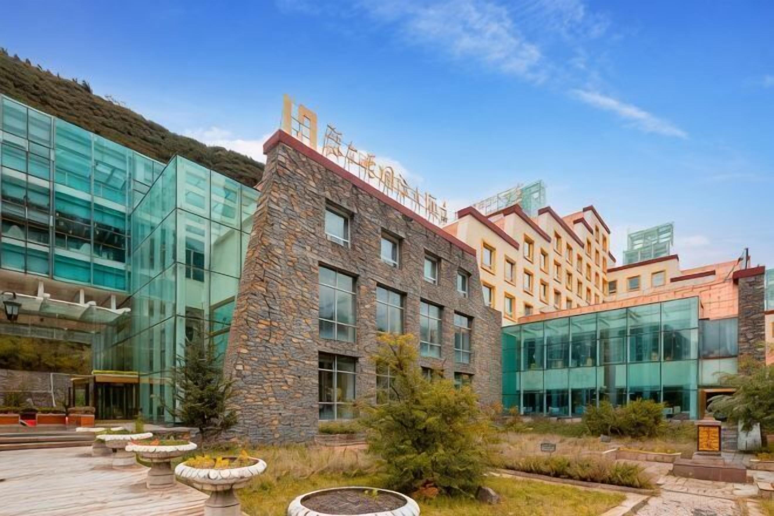 A modern building with a glass facade, stone accents, and a courtyard with planters.