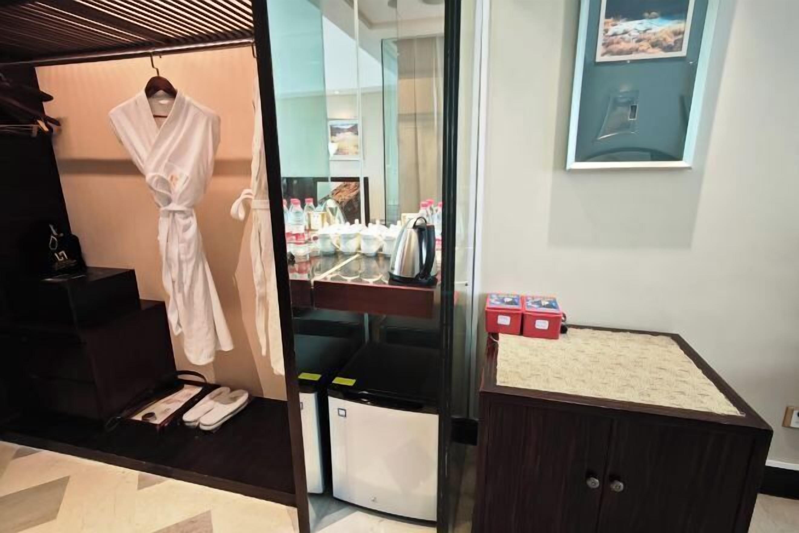 Habitación de hotel con bata colgada, espejo, lavamanos con artículos de aseo y un mueble pequeño.