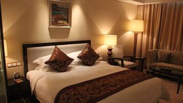 A hotel room with a large bed, two bedside lamps, a chair, and a painting on the wall.