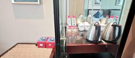 A hotel room with a bed, a small rug, a mirror, a coffee station with kettles, and a window with a view.