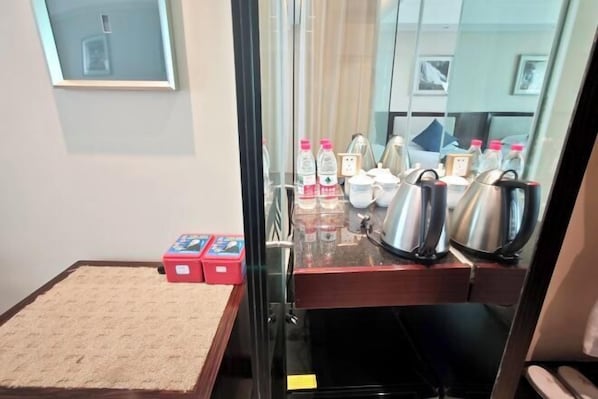 Habitación de hotel con cama, una alfombra pequeña, espejo, estación de café con hervidores y ventana con vistas.