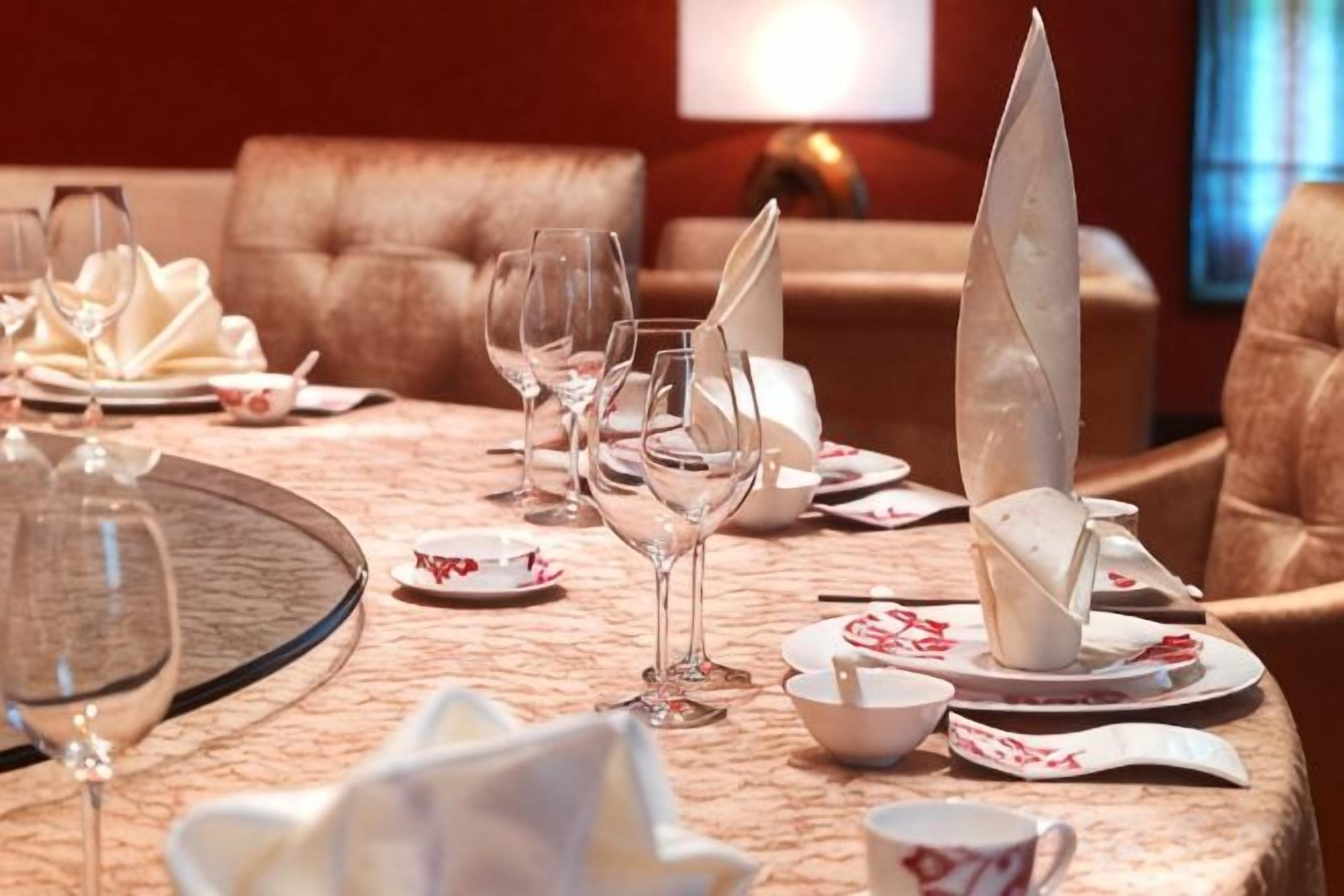 A dining table set with plates, glasses, and folded napkins in a room with a sofa and a lamp.