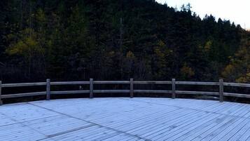 A wooden deck with a railing, surrounded by a forested hillside.