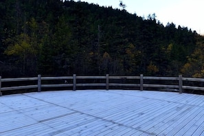 A wooden deck with a railing, surrounded by a forested hillside.