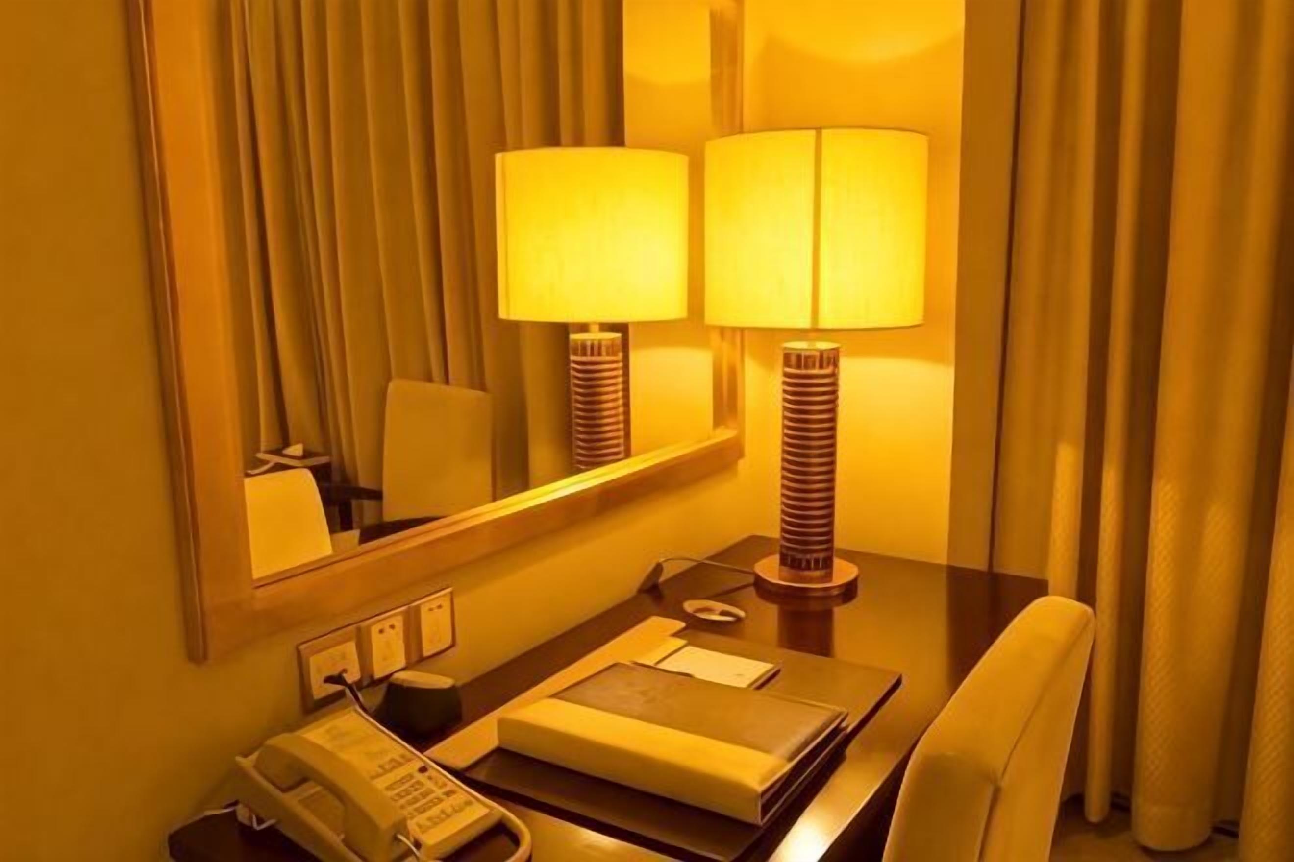 A hotel room with a desk, two lamps, a telephone, and a mirror.