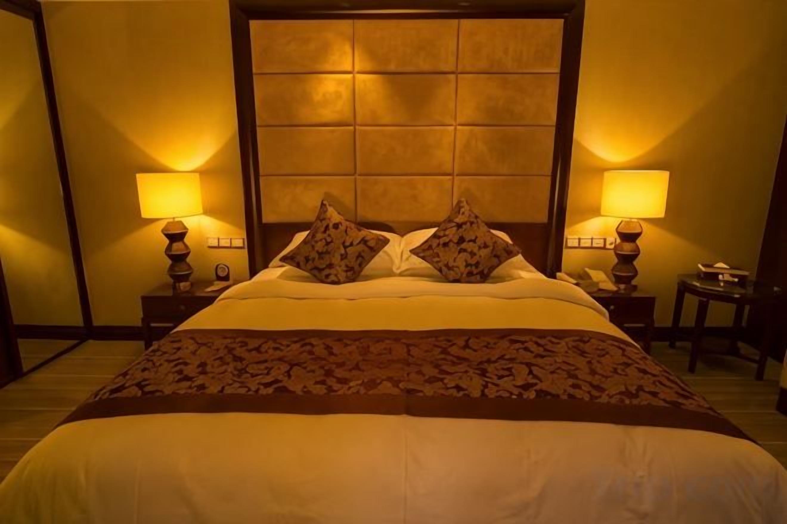 A hotel room with a large bed, two bedside lamps, and a nightstand with a lamp.