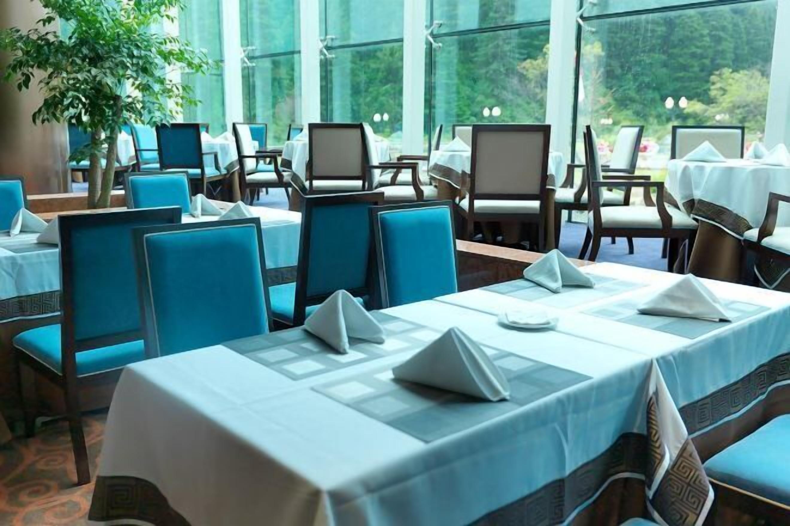 A restaurant with tables set for dining, chairs, and a view through large windows.