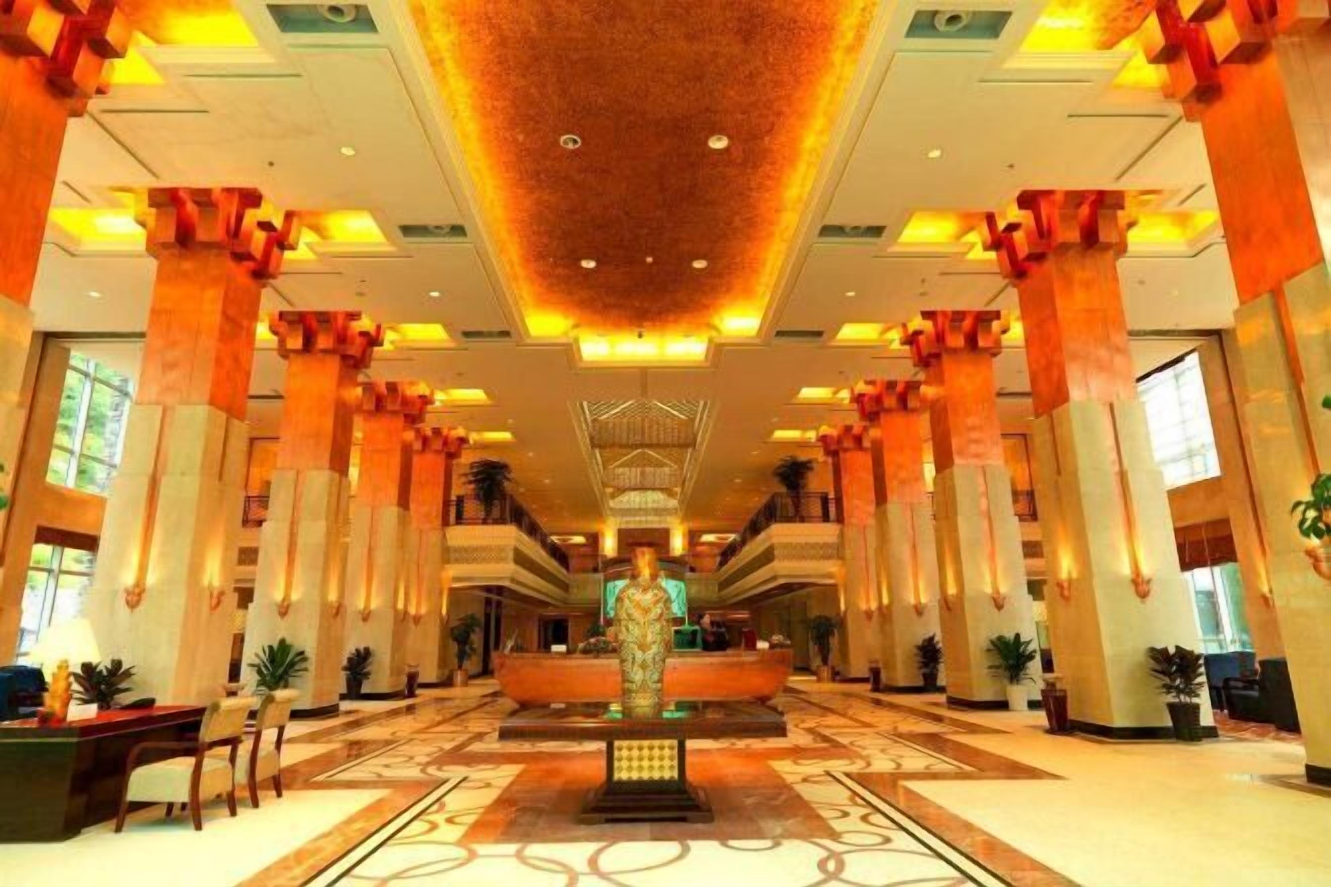 Eine Hotelhalle mit einer zentralen Rezeption, mehreren Säulen und einem gemusterten Boden.