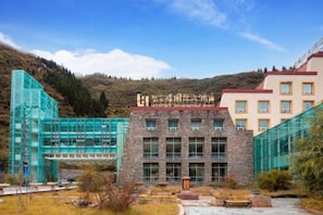 A hotel with a modern glass facade, a stone building with large windows, and a mountainous backdrop. - Seercuo International Hotel (Songpan)