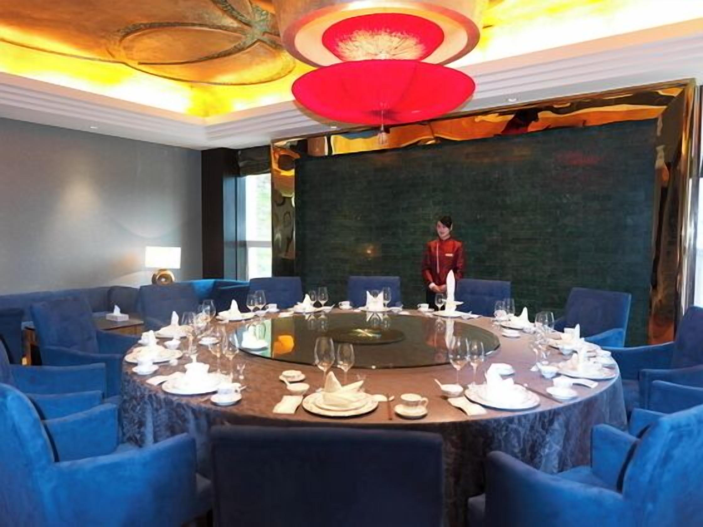 A conference room with a round table, blue chairs, and a person standing at the table.