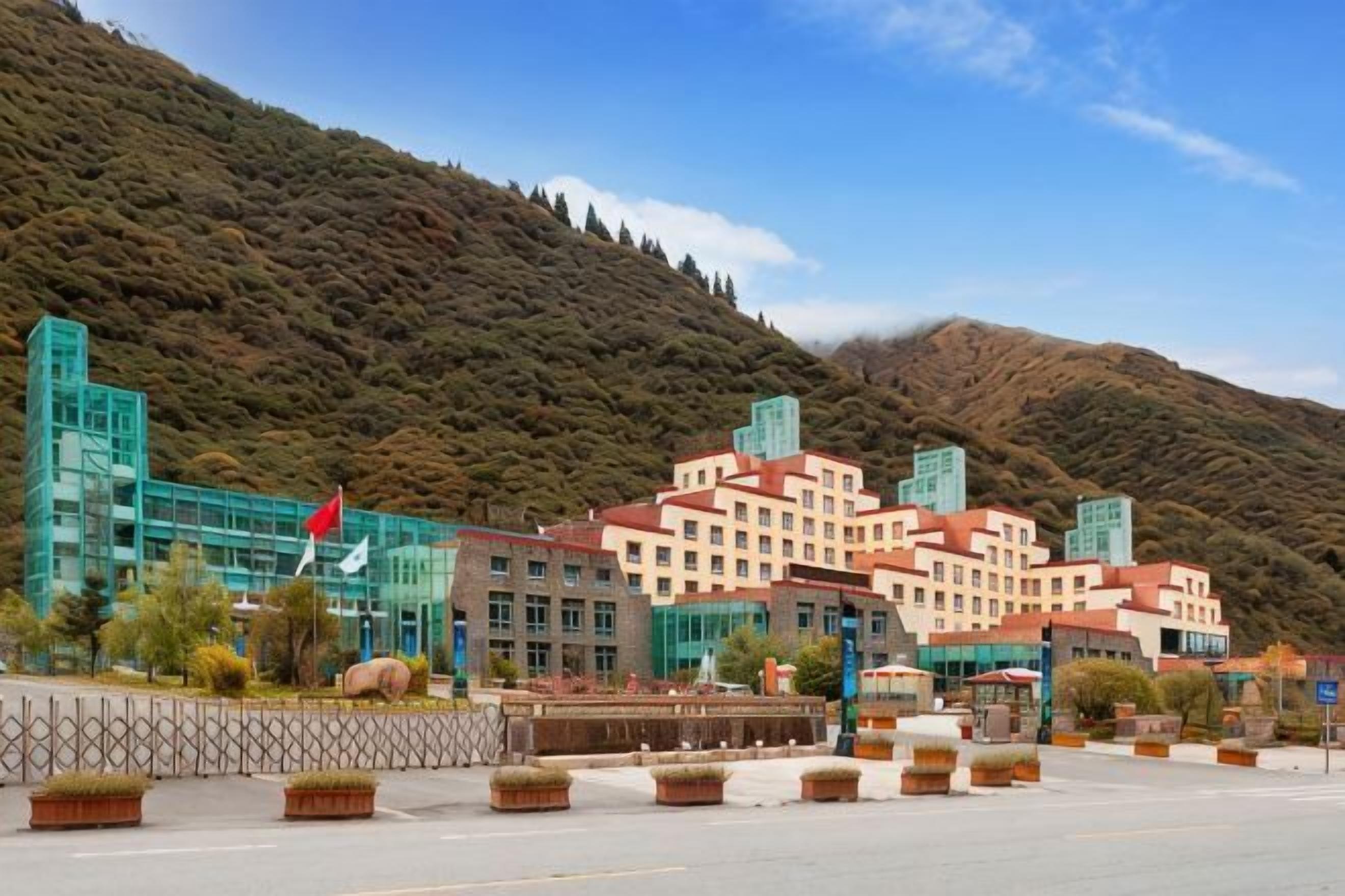 Un hotel de varios pisos, una bandera y un paisaje montañoso de fondo.