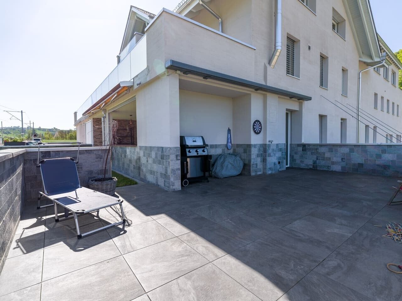 Eine überdachte Terrasse im Freien mit Grill, Klappstuhl und kleinem Tisch.