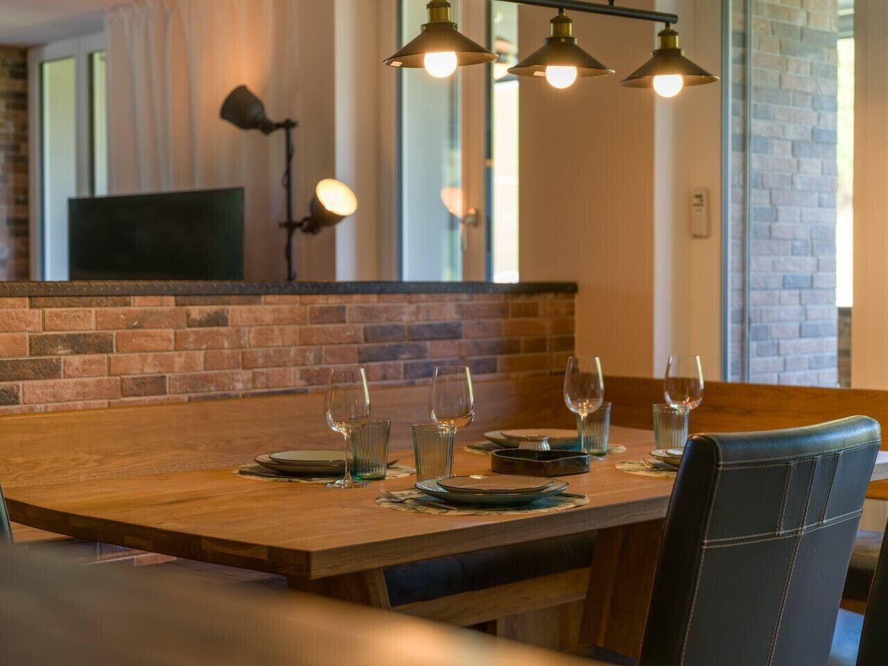 A dining area with a wooden table set for four, a brick wall, and pendant lighting.