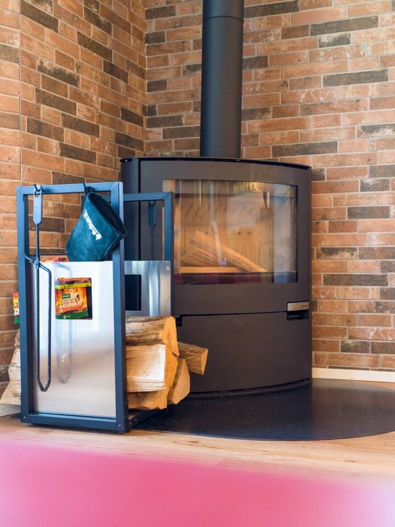 A modern wood-burning stove with a glass door, a stainless steel refrigerator, and a blue-framed storage unit with a black pot on top.