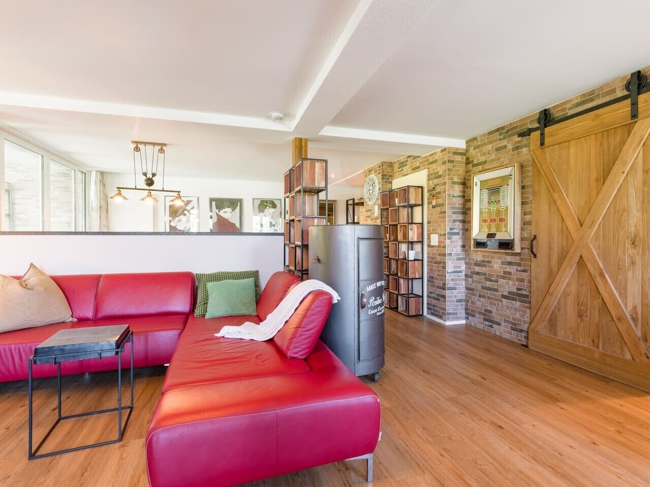 A spacious living area with a red sofa, a coffee table, and a fireplace. There is a brick wall with a wooden door and a large window.