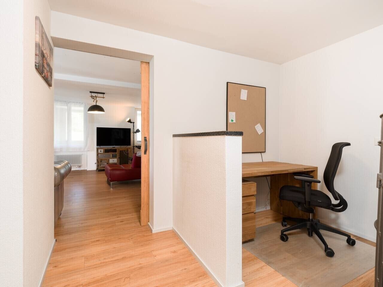 Una habitación con un escritorio de madera, una silla de oficina negra y un tablón de corcho en la pared.