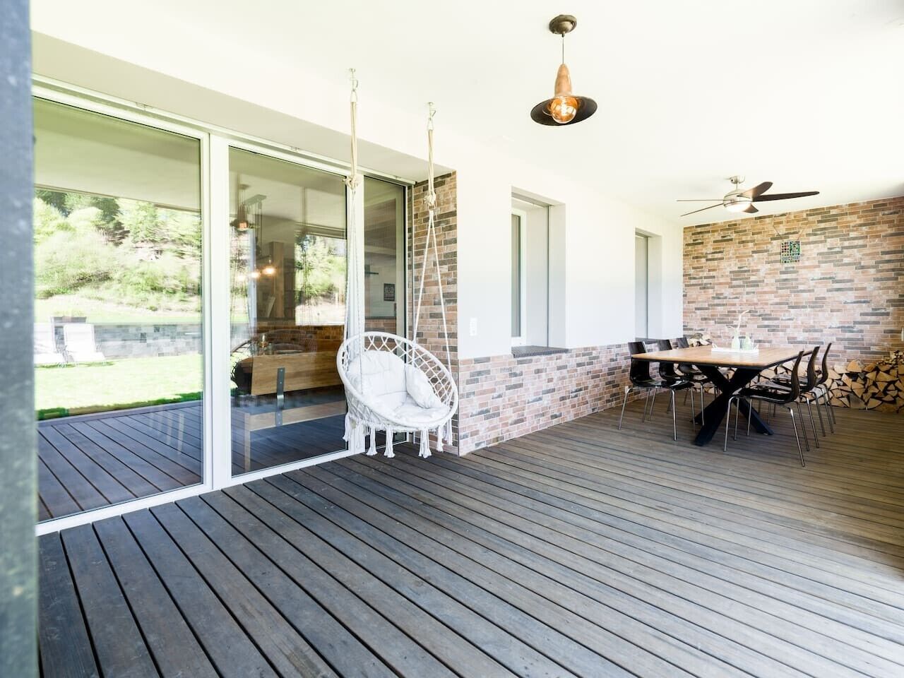 An outdoor deck with a dining area, a hanging chair, and a brick wall.