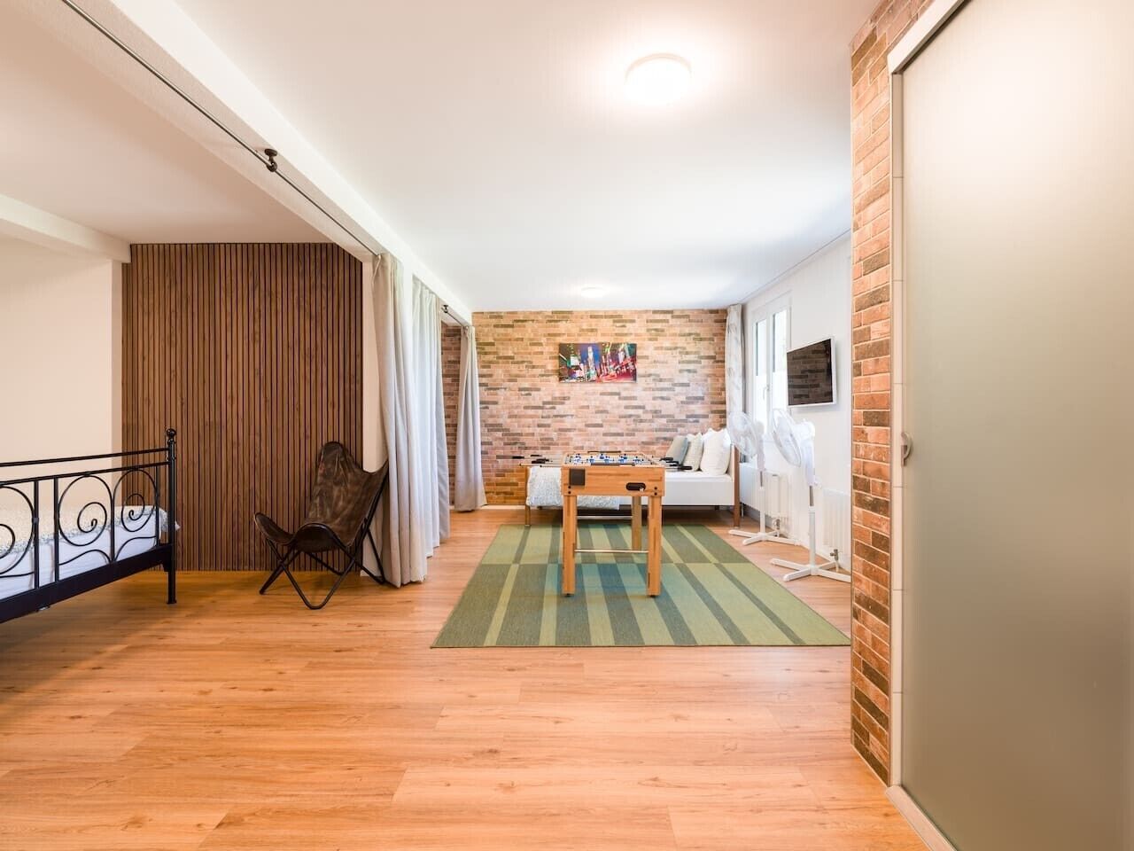 Een kamer met een houten vloer, een bank, een tafel en een tafelvoetbal.