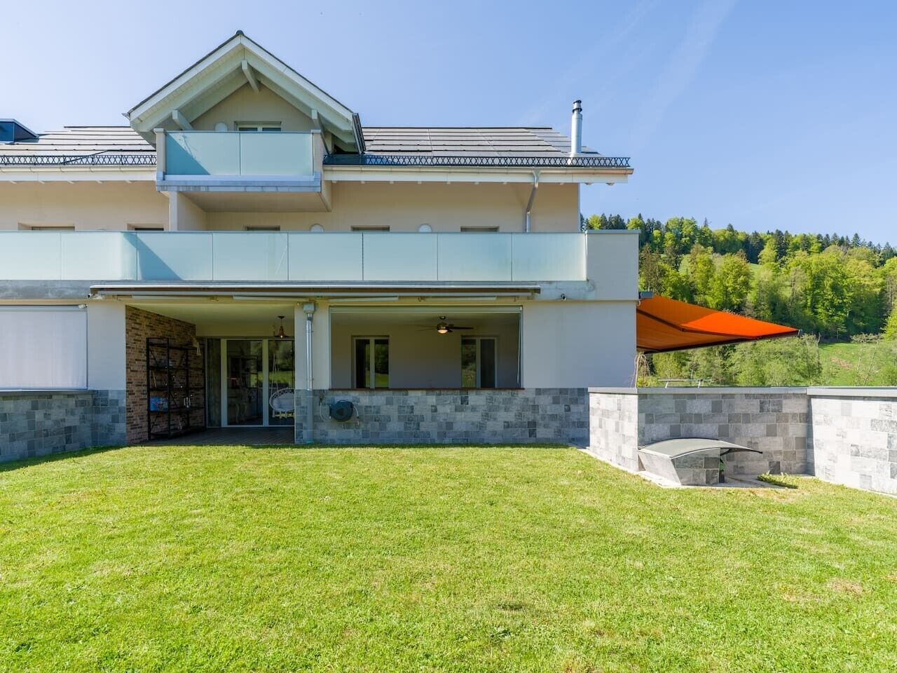A modern two-story house with a covered patio and a stone wall.