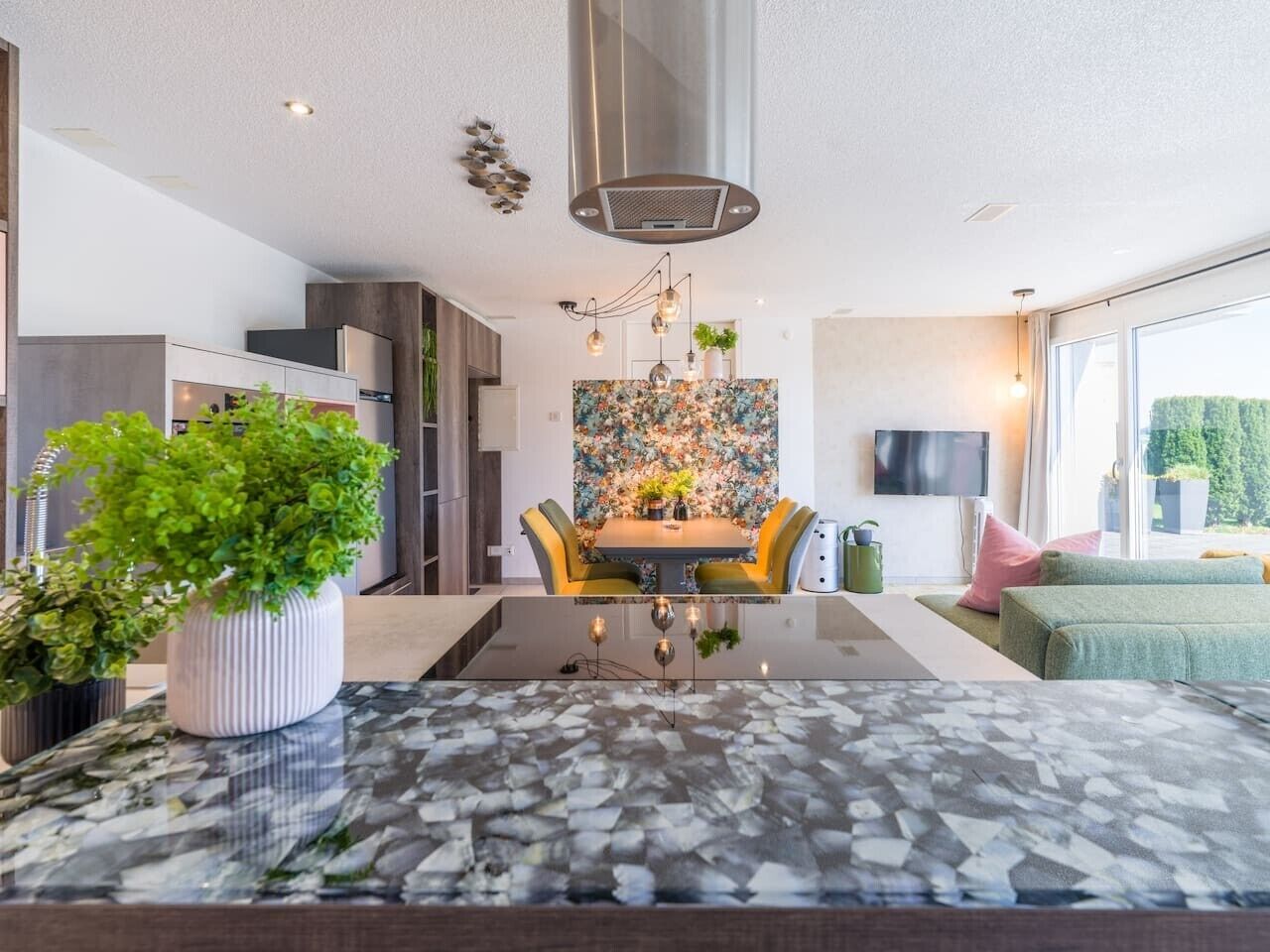 Eine moderne Küche mit Kochinsel, Essbereich und Wohnbereich mit Sofa und Fernseher.
