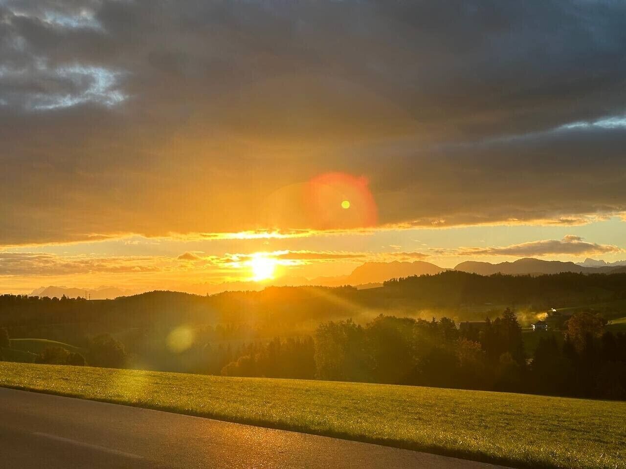 Pôr do sol sobre uma paisagem acidentada, com uma estrada em primeiro plano.