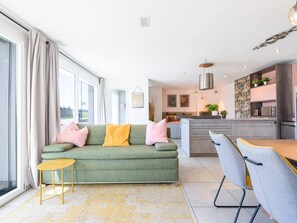 A modern living room with a sofa, a small table, and a dining area with chairs.