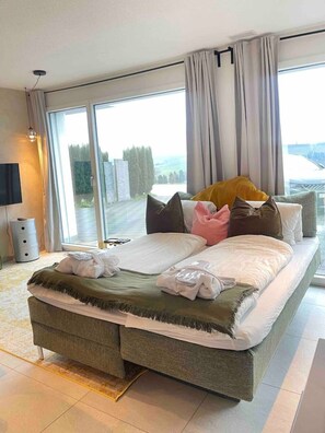 A modern bedroom with a large bed, a flat-screen TV, and a view of the outdoors through a sliding glass door.
