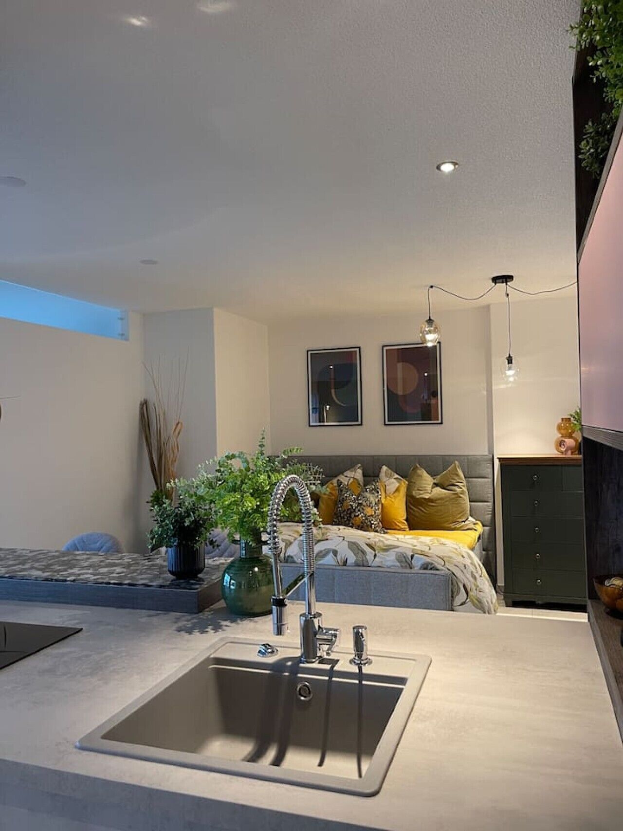 Een moderne keuken met een inbouwspoelbak, een eethoek met een tafel, en een slaapkamer met een bed en kussens.