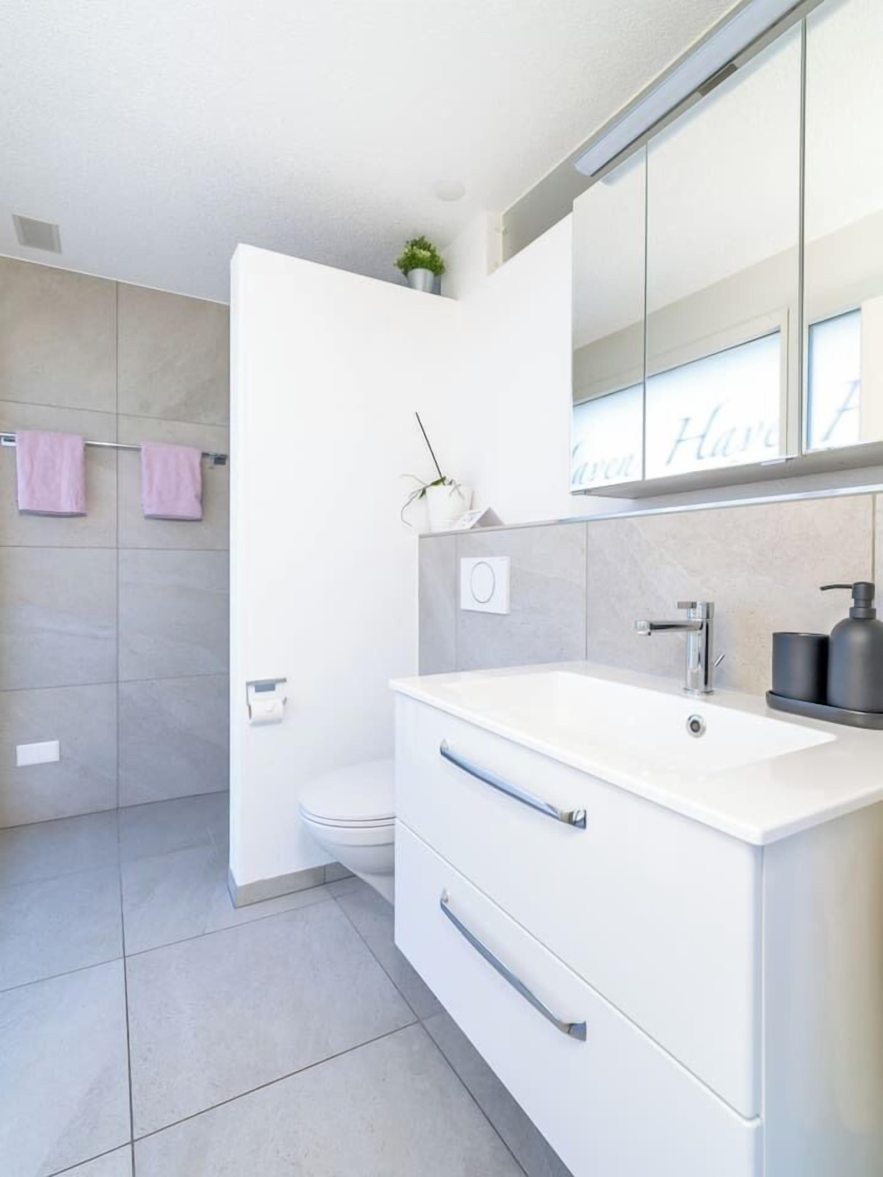 Um banheiro moderno com toucador branco, vaso sanitário e chuveiro.